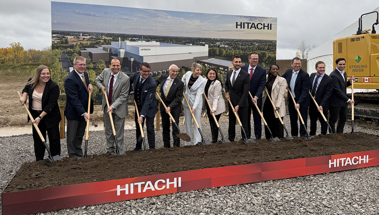 Executives from Hitachi Energy pose alongside Ontario MPPs, federal MPs, and other dignitaries while breaking ground at a ceremonial construction site.